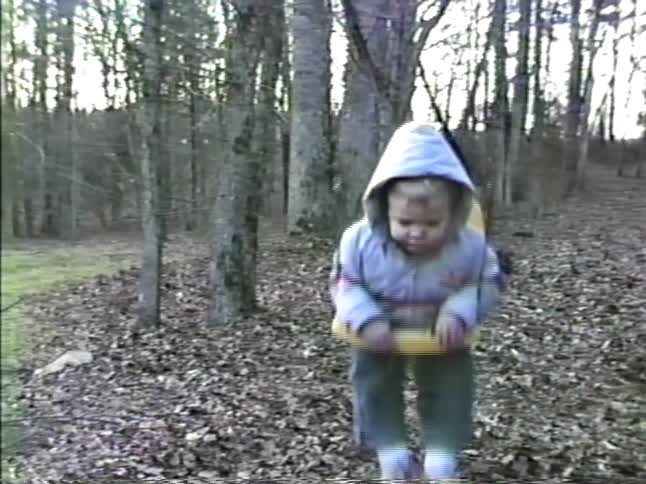 A boy pushes his toddler brother in a swing near a forest