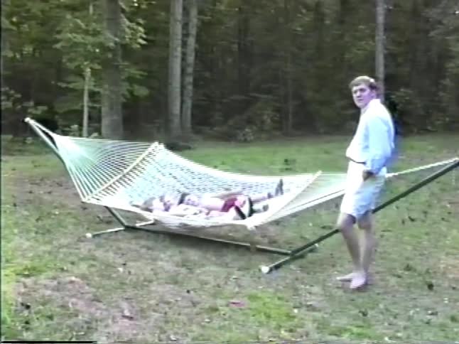 Father smiles while standing in a field next to the hammock his children are swaying in on a summer day