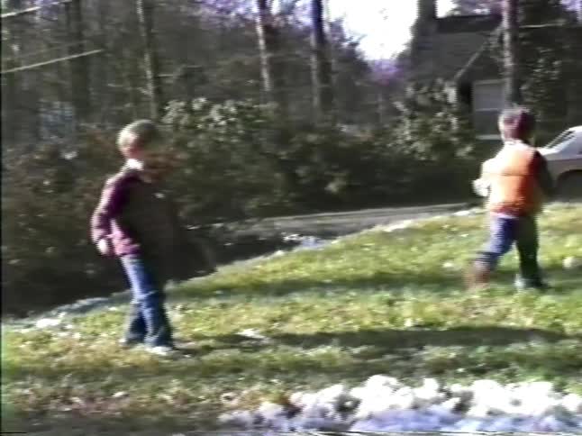 Children playing baseball on a residential lawn with parked cars in the background