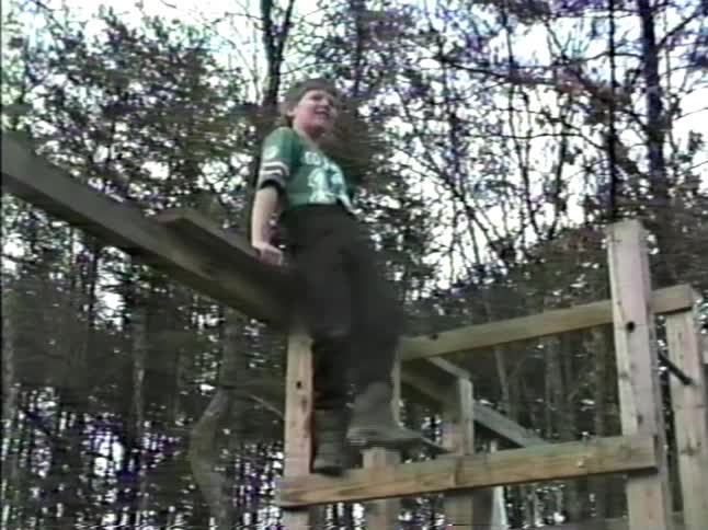 Nostalgic home movie footage of children playing on a wooden backyard playset including a toddler in a swing and an older boy waving from a high beam