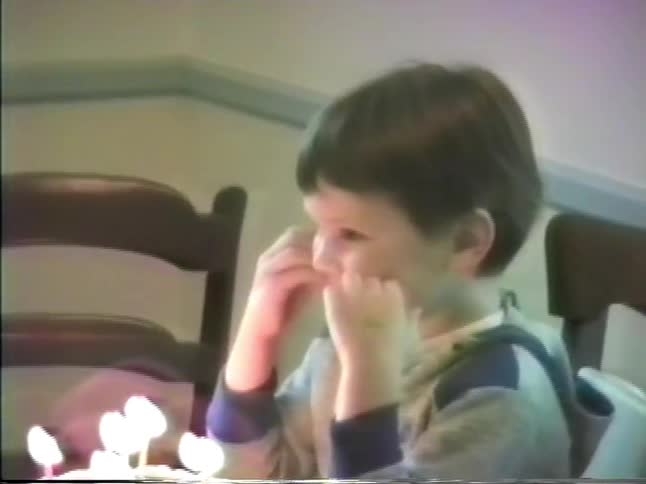 Father presents birthday cake to his son and the boy blows out the lit candles