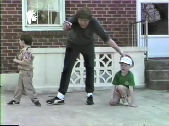 A father teaches his two young sons how to get into a football stance on their back patio
