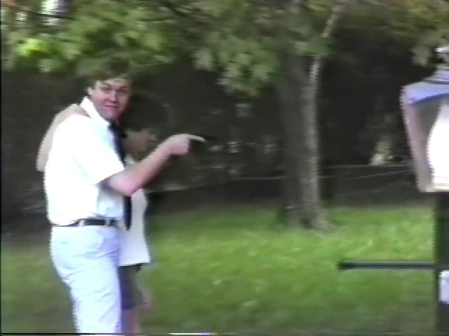 Man and woman standing in their yard holding hands and their children play as they walk away with their arms around each other