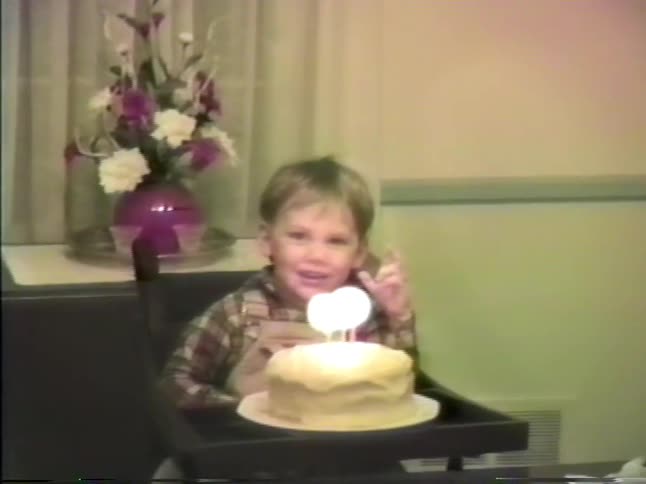 A mother lights the candles on a birthday cake for her small son