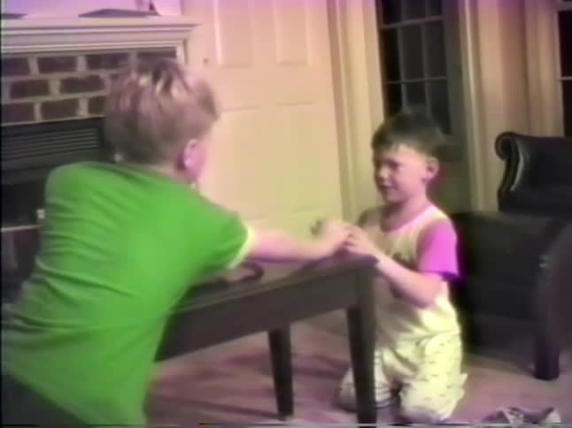 Two young boys play a game with each other by flicking a folded paper