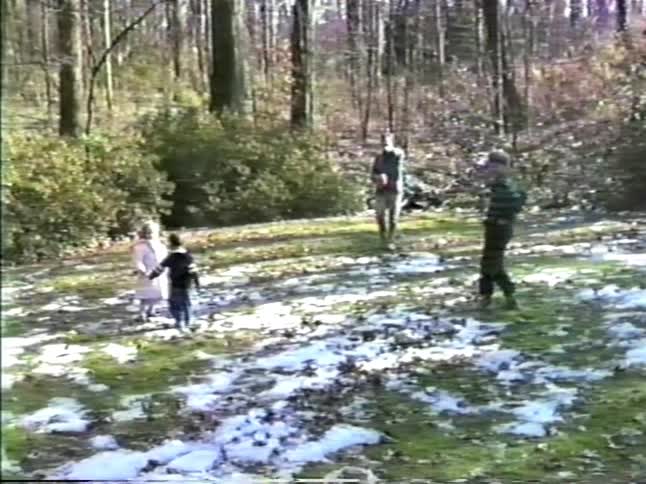 Boy plays football catch with his father as his little sister falls in the snow in the yard