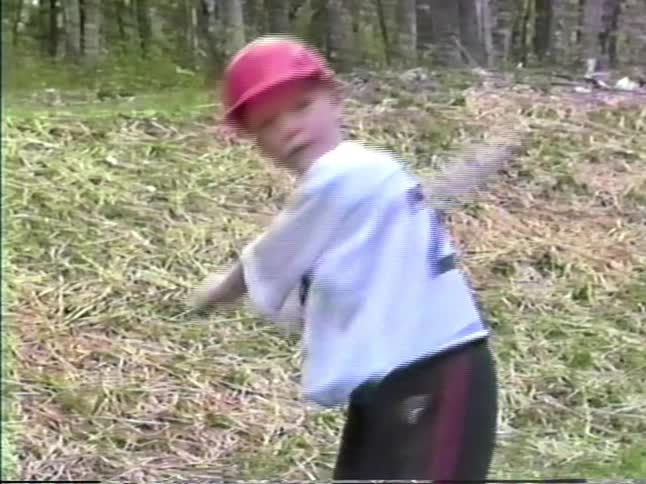 Child holding a bat in a grassy area with trees in the background