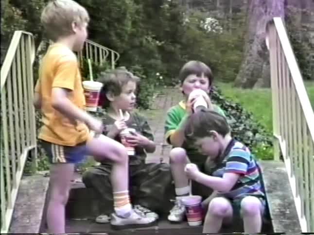 Four kids sitting on a stairway walkway at midday drinking milkshakes and having fun together