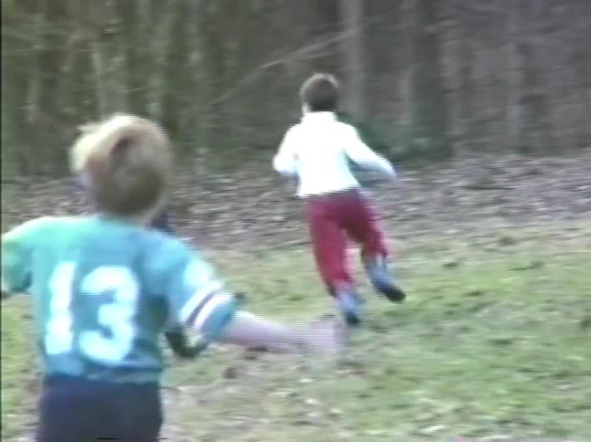 Some young boys playfully chase each other around a large yard