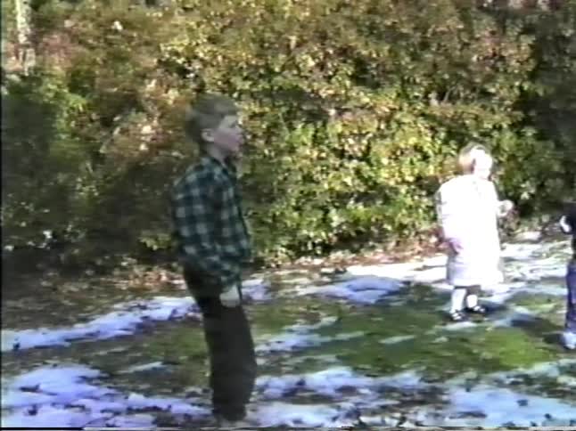 Children playing outdoors on a lawn with scattered snow and vegetation in the background