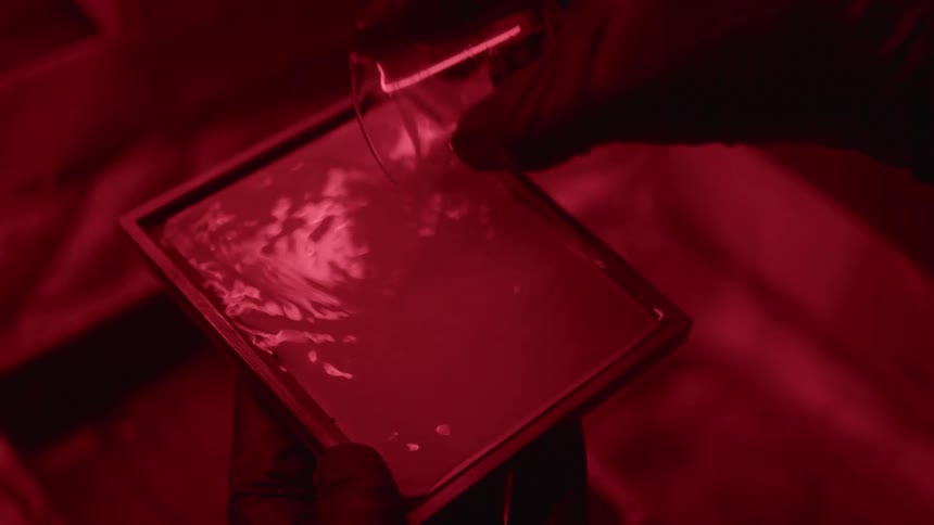 Photographer pouring solution into a container developing pictures under a red light in the darkroom
