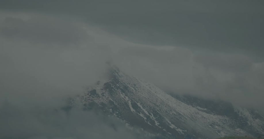 Clouds move over a partially snowcovered mountain
