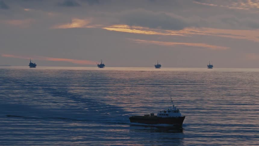 Ship sails on the water with oil rig offshore platforms in the distance