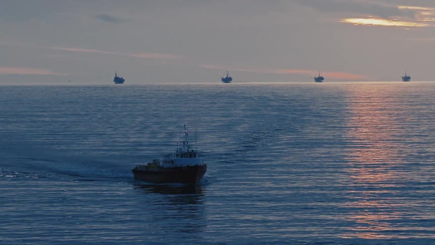 A ship sailing across the ocean at sunset leaving a trail of waves behind it