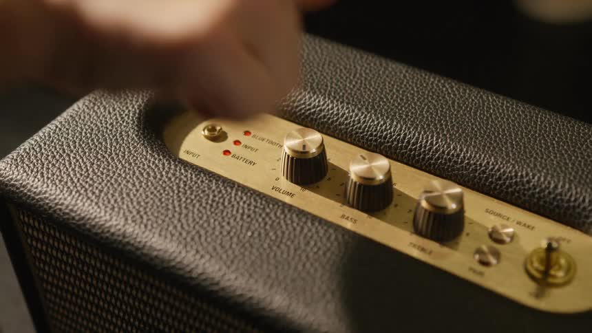 Persons hand turns the volume dial on an audio amplifier radio speaker