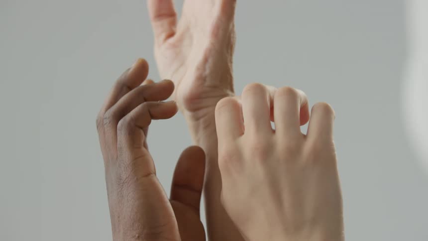 Human hands of different skin tones reach toward each other against a neutral background fingers slightly curled and almost touching