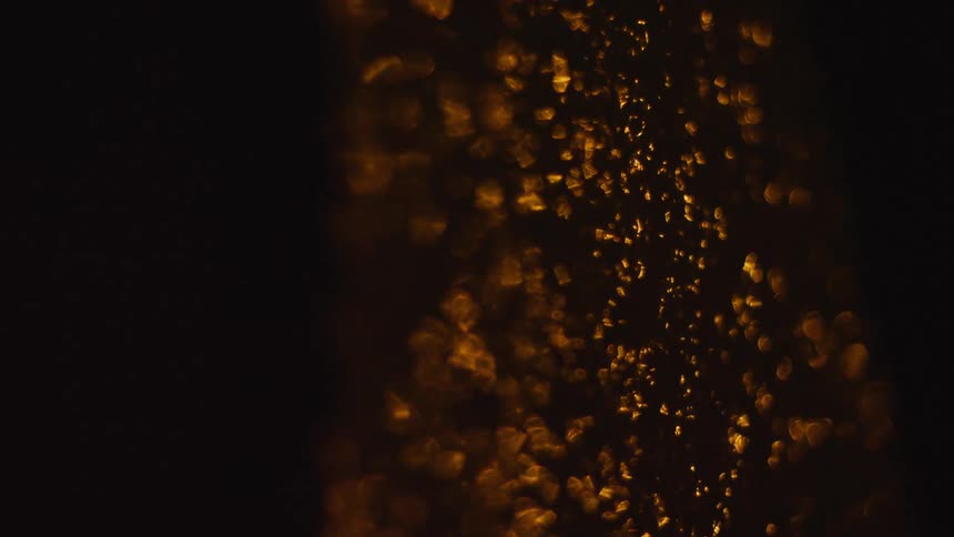 Golden out of focus light particles float and shimmer against a dark background