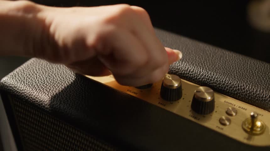 Persons hand turns the volume dial on an audio amplifier radio speaker