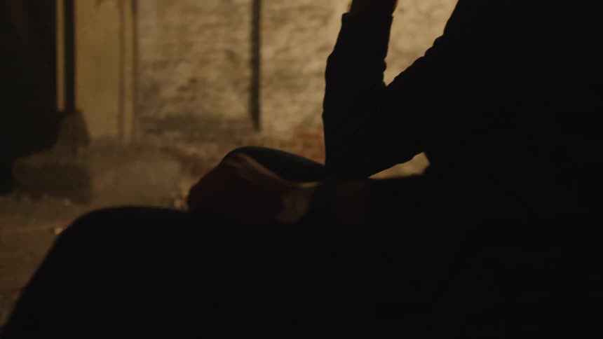 Silhouetted person holding a thin object near the mouth in an indoor setting with a lit wall