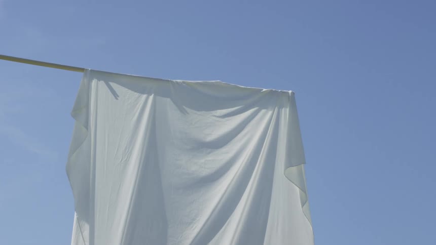 A large white fabric sheet hangs loosely from a horizontal pole billowing gently in the breeze against a clear blue sky