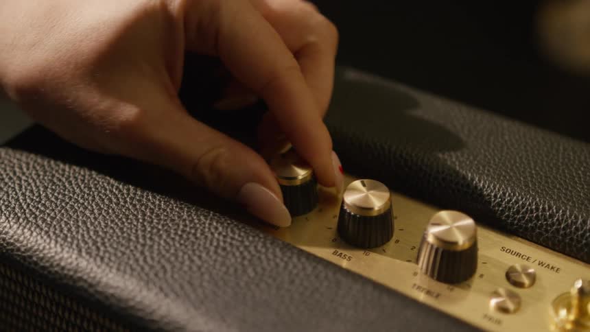 The video shows a closeup of a vintagestyle marshall speaker featuring gold control knobs and a textured black leatherlike finish a hand with long nails reaches into the frame to turn the volume knob up and then quickly pulls away