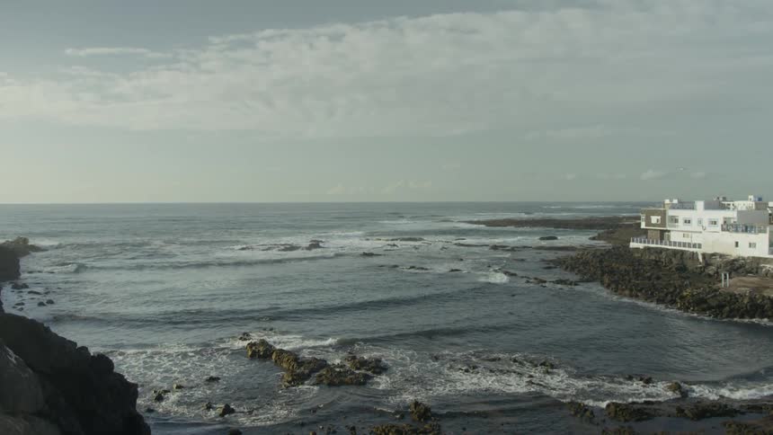 Rocky coastline with ocean waves and seaside buildings in the background