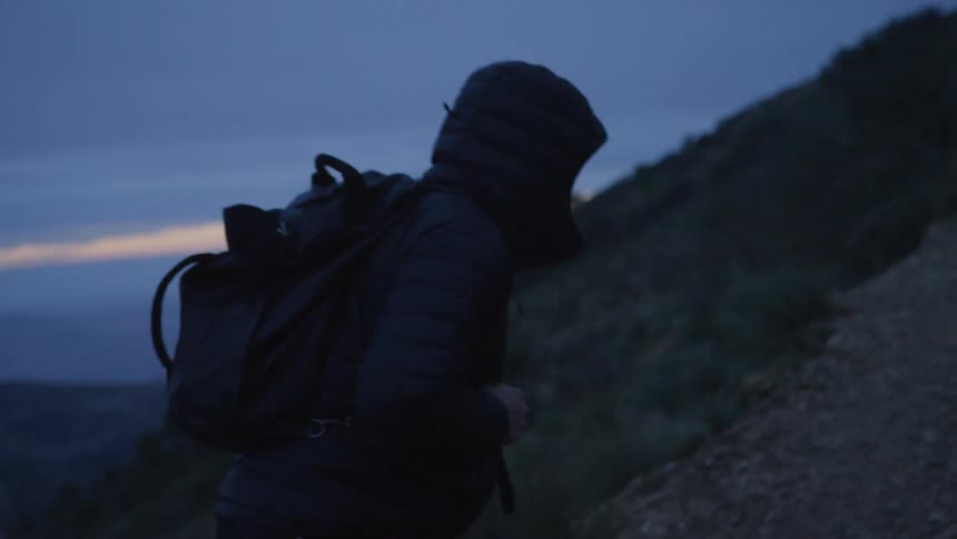 Hiker wearing a hooded jacket and backpack walks up the side of a mountain
