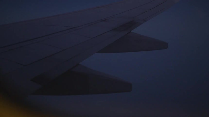 An airplane wing extends into a dark twilight sky as seen from a passenger window during a night flight
