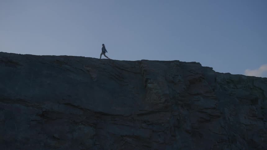 Woman walking along the edge of a mountain cliff