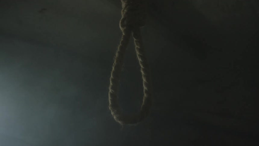 A noose made of coarse rope hangs motionless in dim shadowy light isolated against a dark background that creates a stark somber and unsettling atmosphere