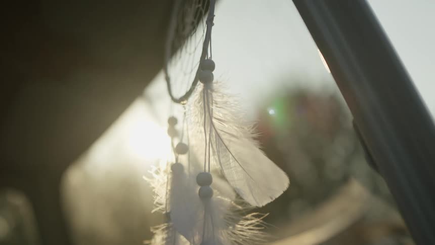 Dreamcatcher feathers Hanging Inside Car with Sunlight Flares – Spiritual Travel Detail Shot
