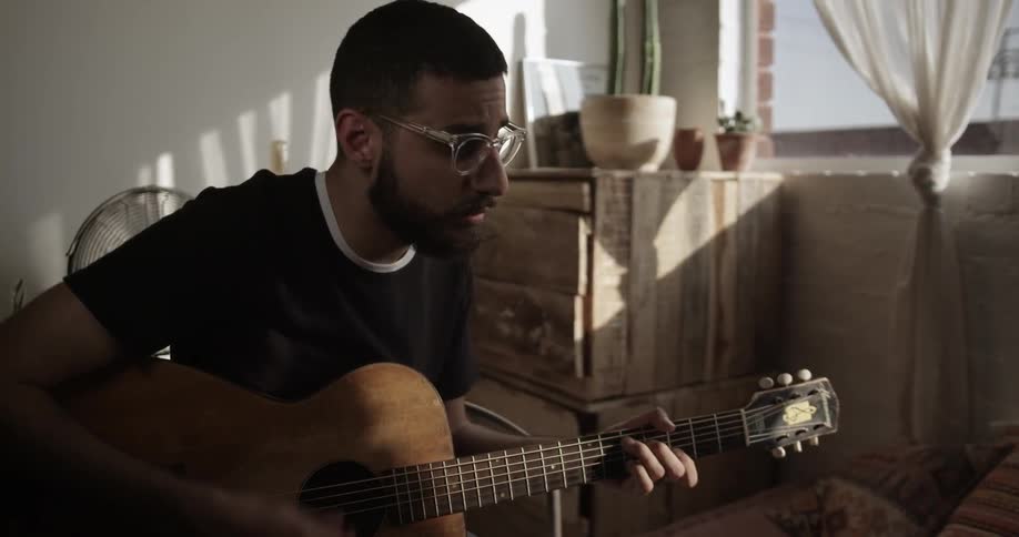 A man plays guitar near the light of a window