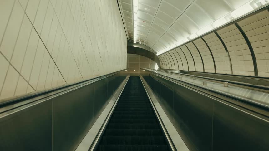 Escalator descends through an underground corridor with curved walls and continuous lighting