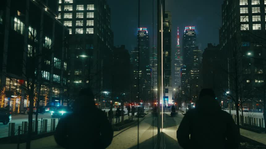 Building facade reflects a pedestrian near a sidewalk on a busy downtown street on a winter night