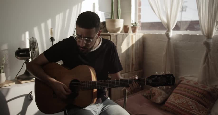 A man plays guitar by a window