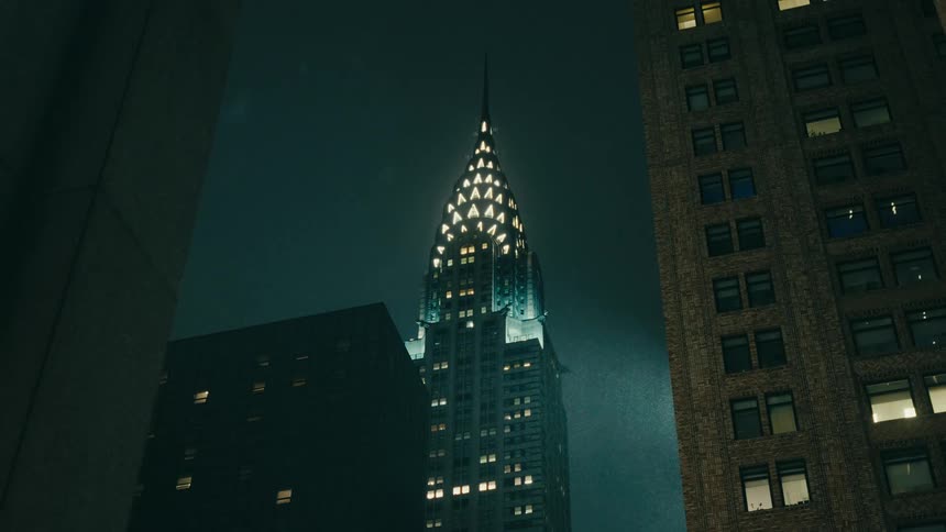 The chrysler building is lit up at night while its raining