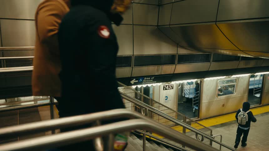 Inside a dimly lit subway station three bundledup commuters descend a metal staircase toward a waiting train as other passengers stand and move along the platform nearby