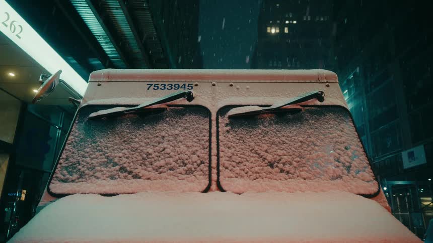 Truck parked at night with windshield covered in snow under urban lighting