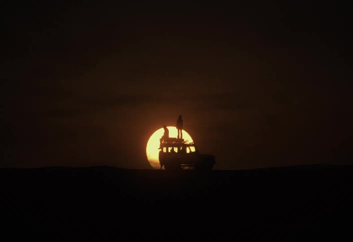 A silhouette of two people on a car at sunset