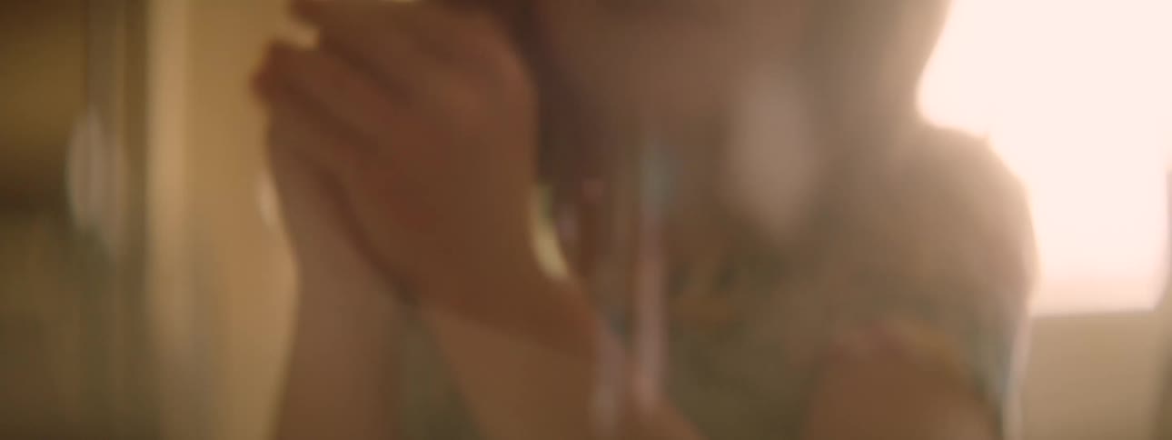 In a room with sun flare beaming a young female shakes he clasped hands and releases them towards a board game on the floor