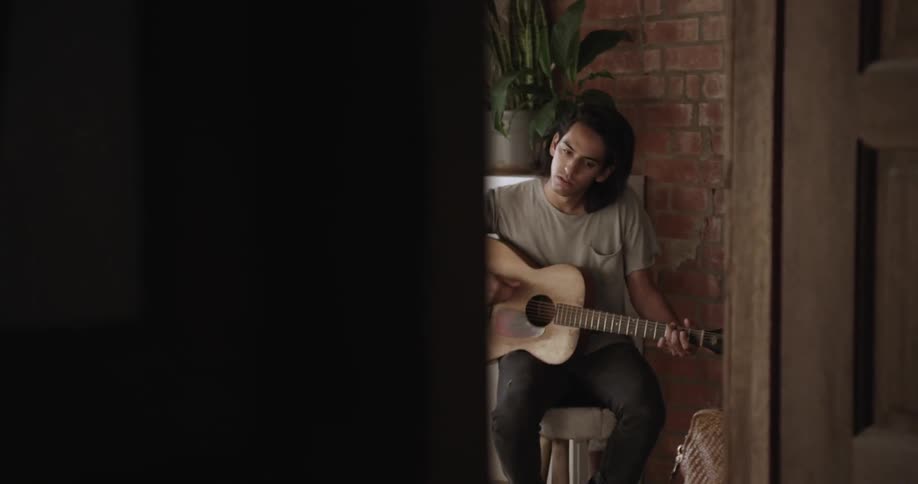 A man sits on a stool and sings while playing the guitar
