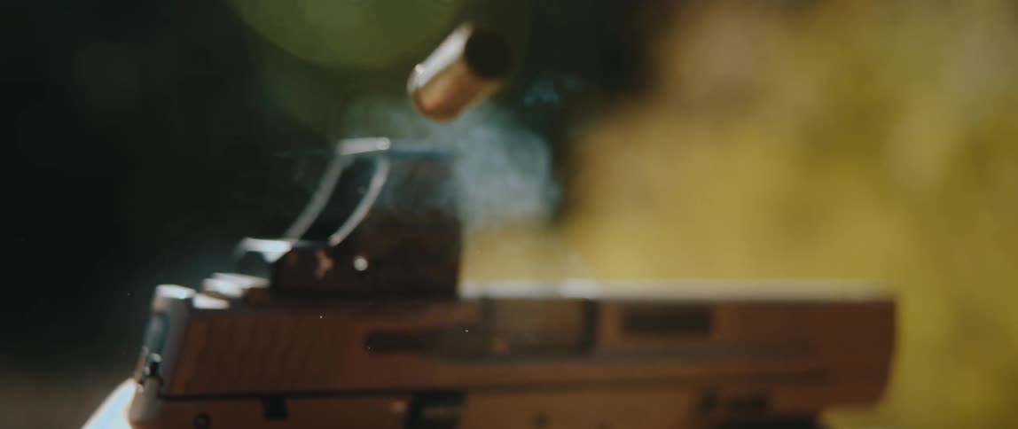 The video shows a closeup slowmotion sequence of a semiautomatic handgun being fireda brass shell casing is ejected from the firearms chamber and tumbles upward through the airwisps of grey smoke trail out of the open slide and drift upward as