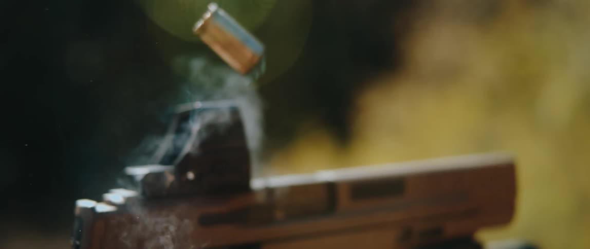 Closeup of a handgun firing with smoke and an ejected casing