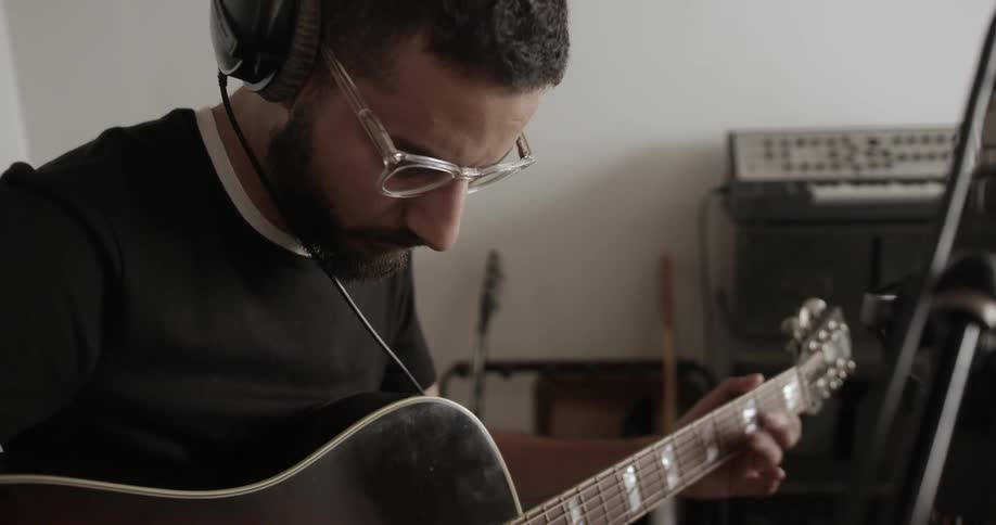 A man is playing the guitar near some equipment