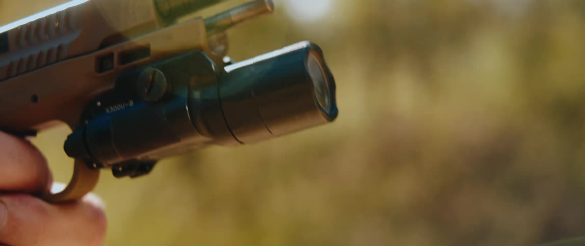 A tan handgun with a mounted flashlight is fired in a closeup shotthe slide cycles back and forth as smoke and a small spark emit from the barrel