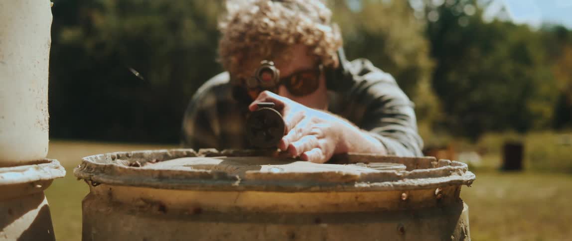 Man leaning over a barrel looking through the scope of his rifle