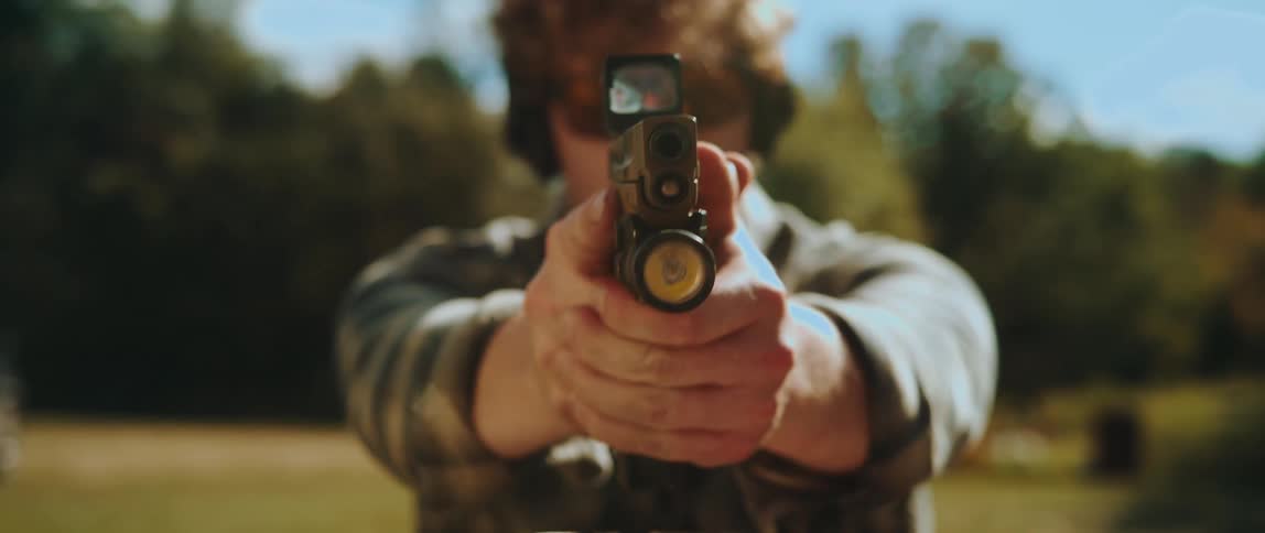 Man in a field pointing a gun