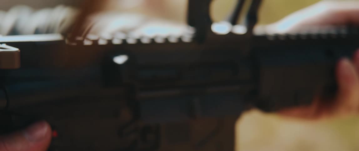 Hands on a rifle firing shots as bullet shells fly into the air