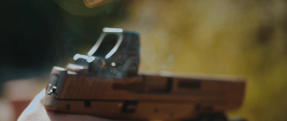 Closeup of a hand firing a handgun as a spent bullet casing ejects outdoors