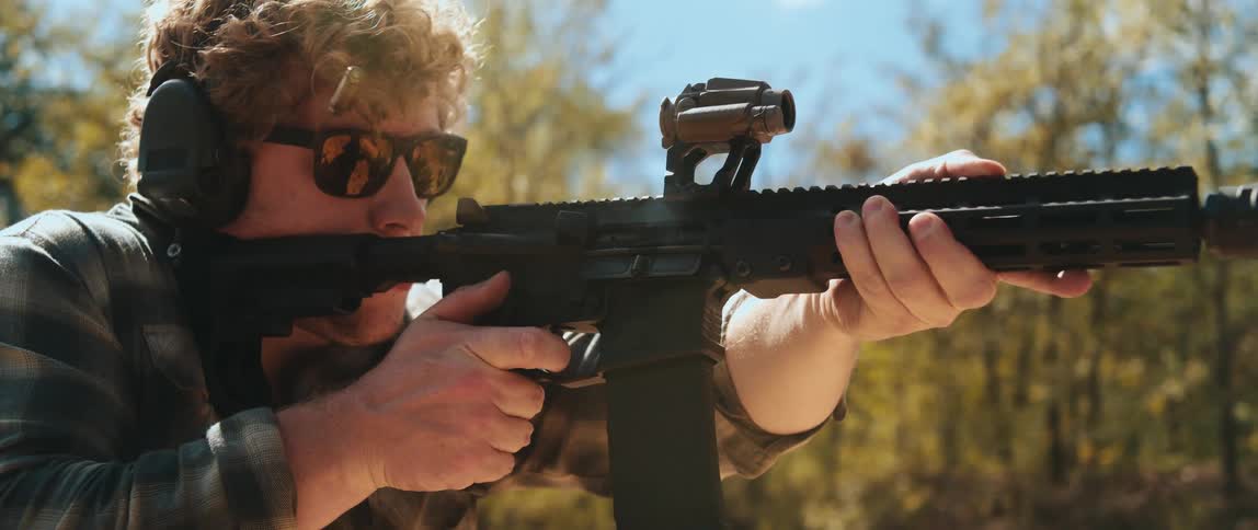Person fires a rifle with a mounted optic during outdoor shooting practice